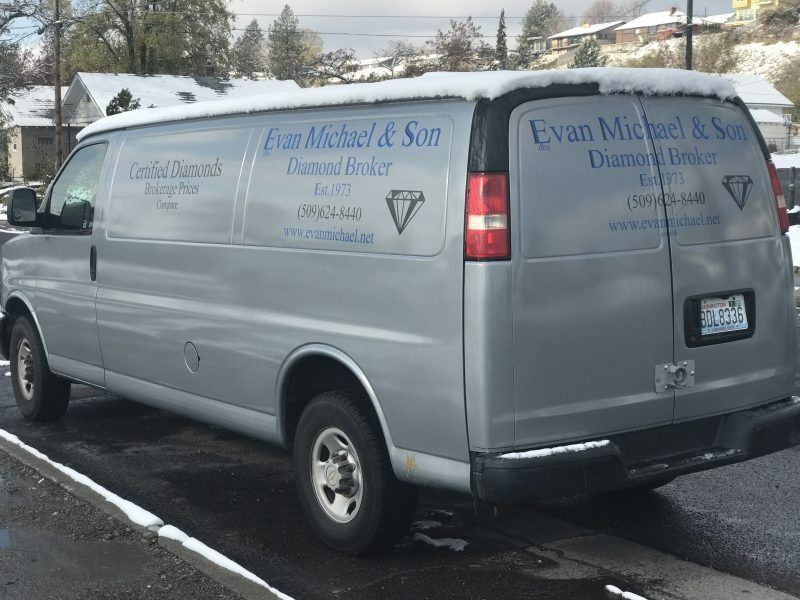 A silver van parked outdoors with snow on its roof, featuring 