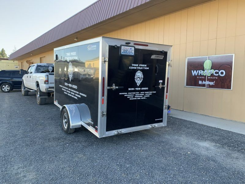 A white pickup truck hitched to a black trailer parked in front of a tan building with a Wrapco sign.