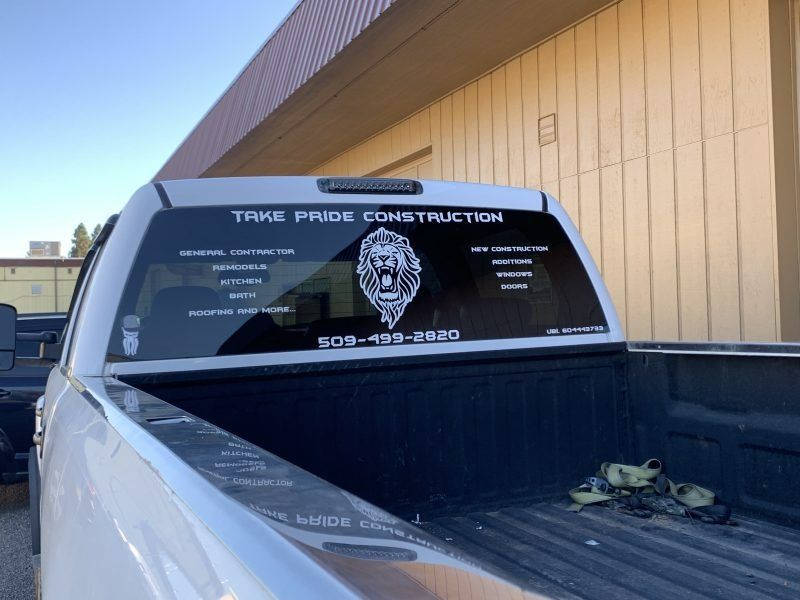 White pickup truck with a decal on the rear window featuring a lion logo, company name, services, and phone number.