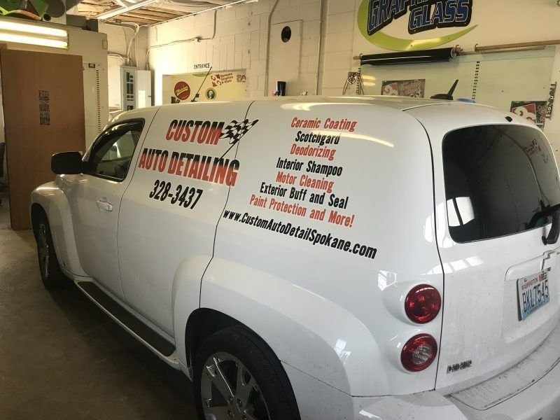 A white van parked indoors with custom auto detailing advertising text on the side.