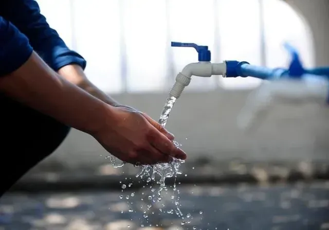 Lavado de manos bajo un grifo azul en un lavabo con agua corriente y espuma de jabón.