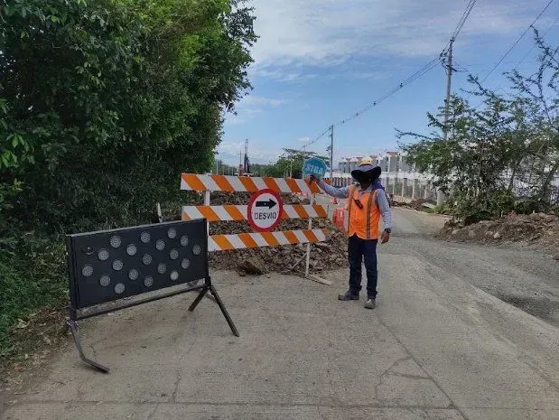 Un control de carretera con barreras a rayas y un trabajador de pie en una carretera cerrada.