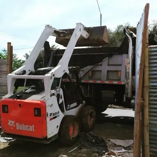 Una minicargadora Bobcat carga escombros en un camión volquete en una obra.