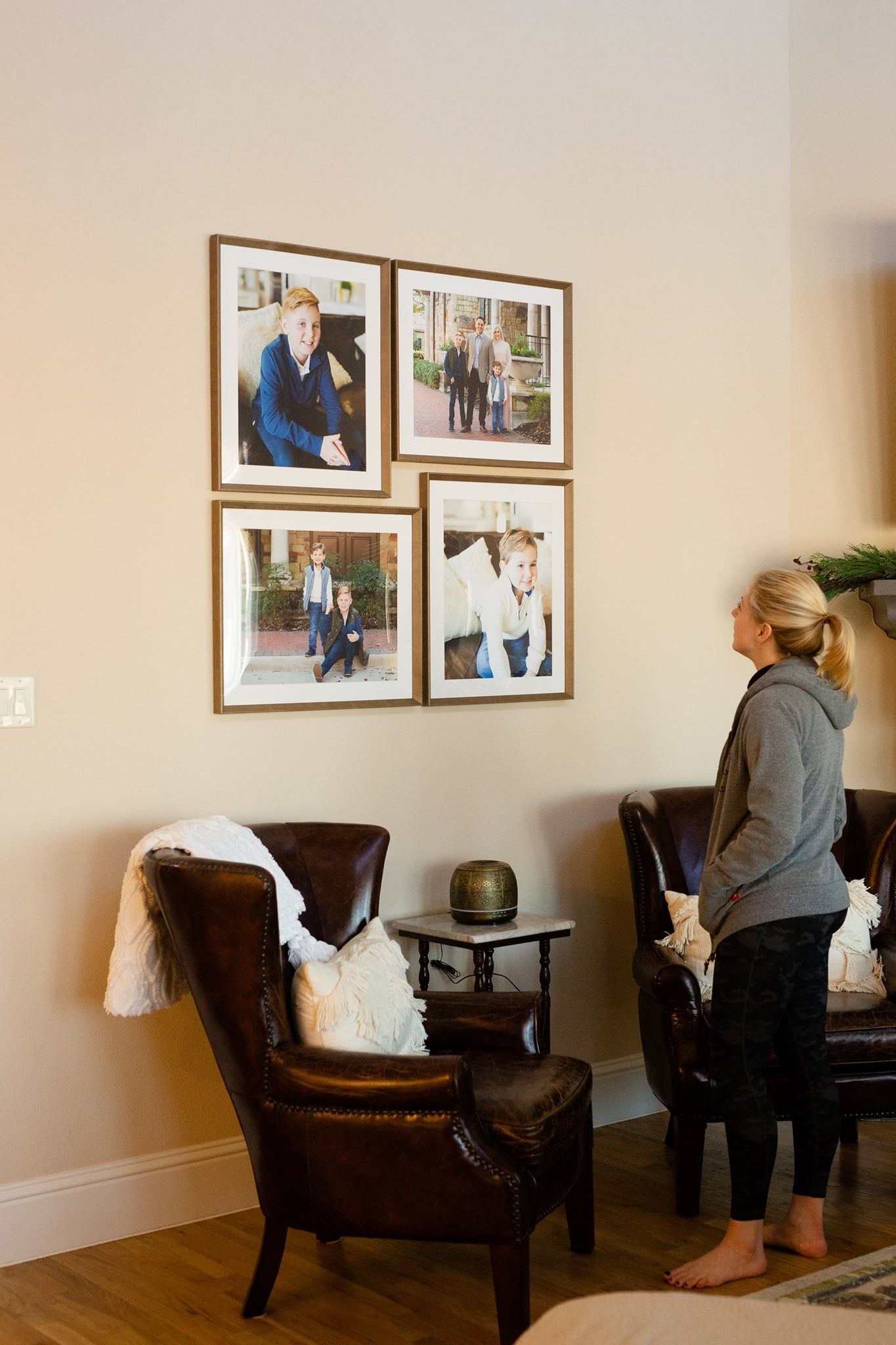 A woman is standing in a living room looking at pictures on the wall.