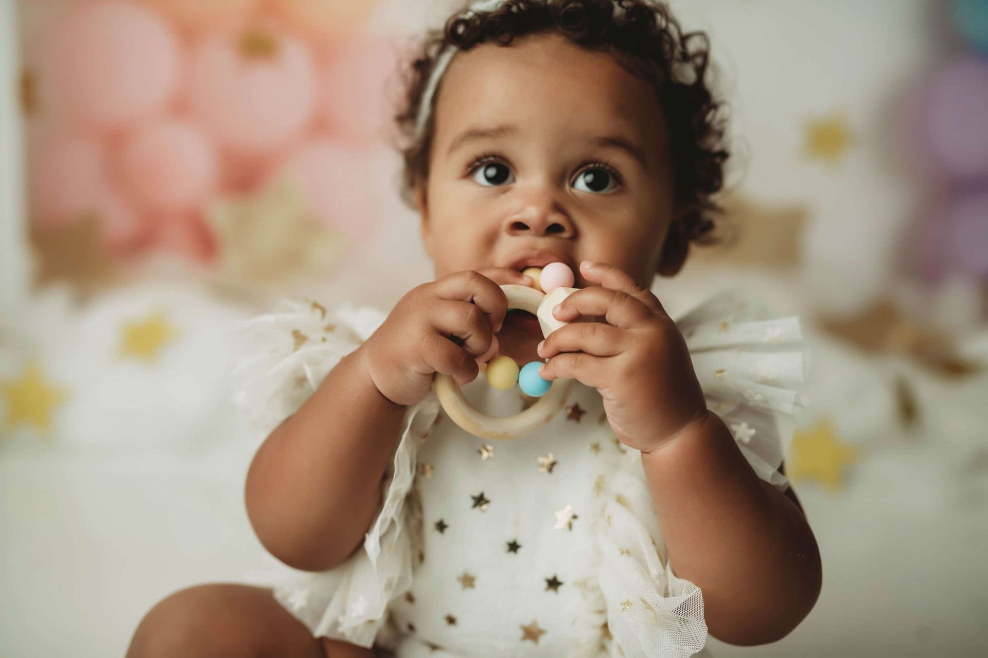 A baby is chewing on a teething ring while sitting on a bed.
