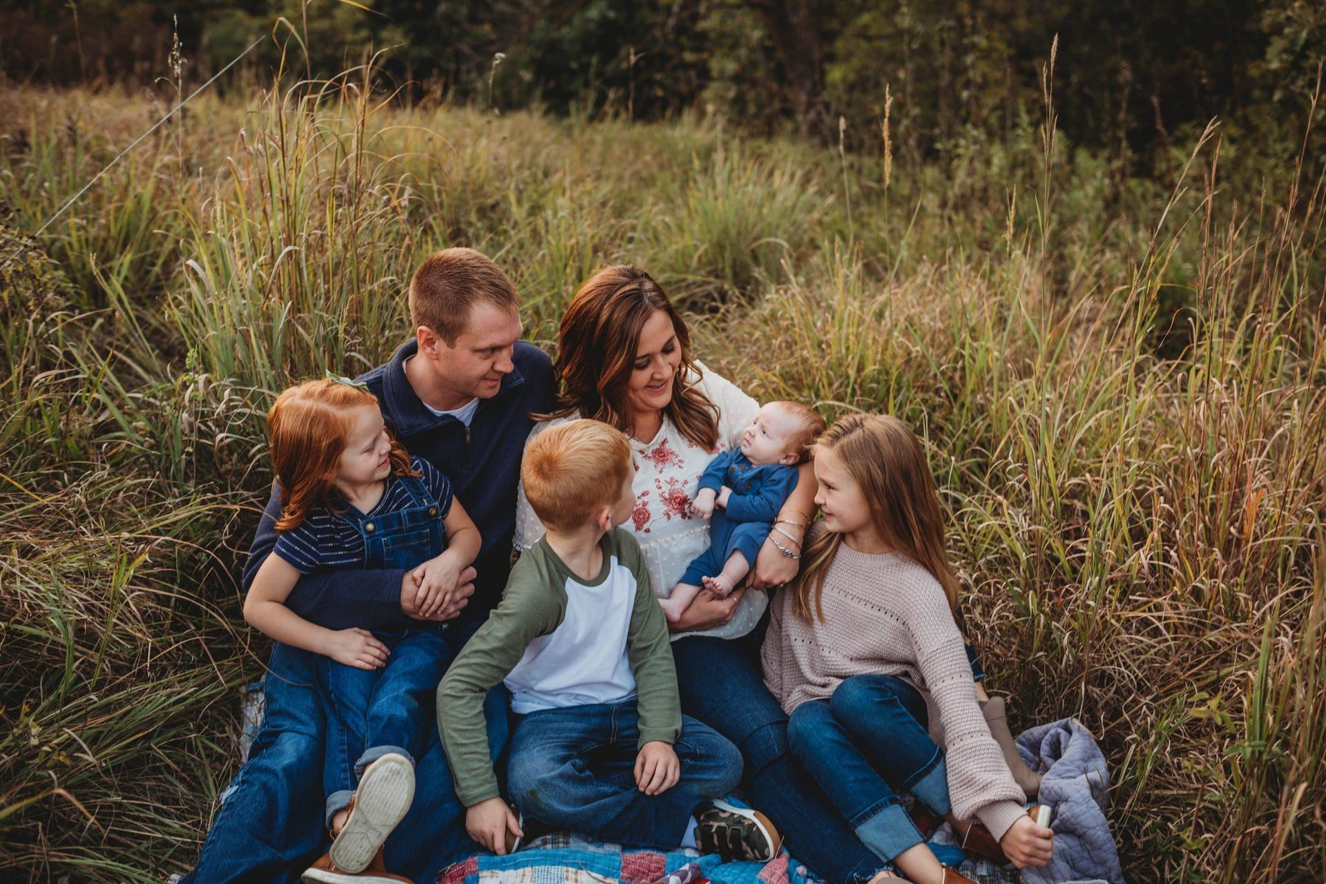 A family is sitting on a blanket in a field.