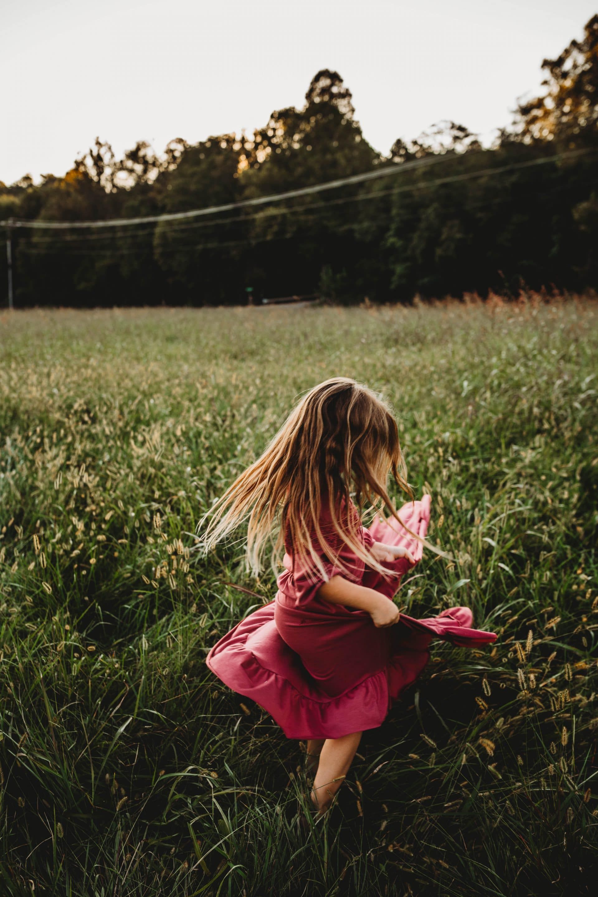 A little girl in a pink dress is running through a grassy field.