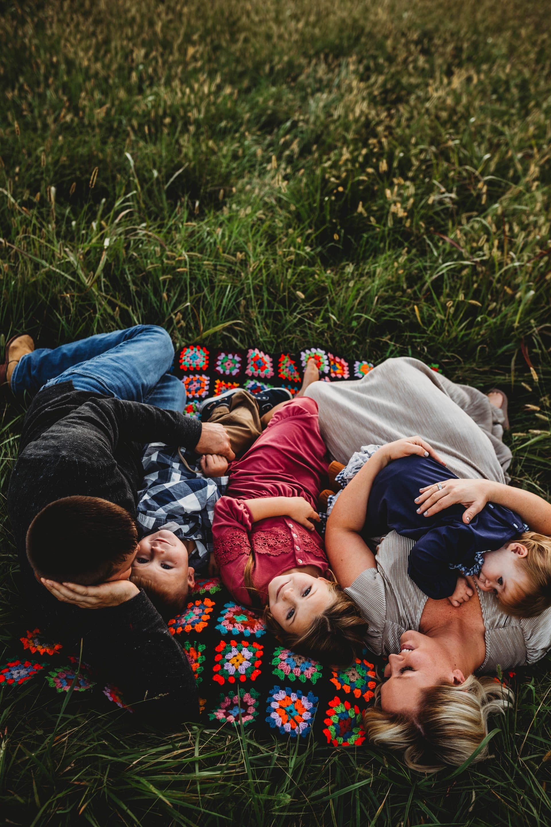 A family is laying on a blanket in the grass.
