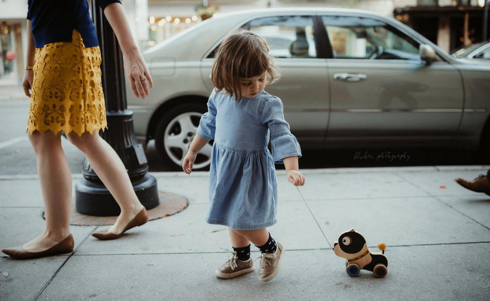 A little girl is walking with a toy dog on a leash.