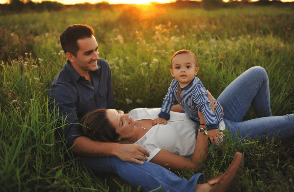 A man and woman are laying in the grass with a baby.