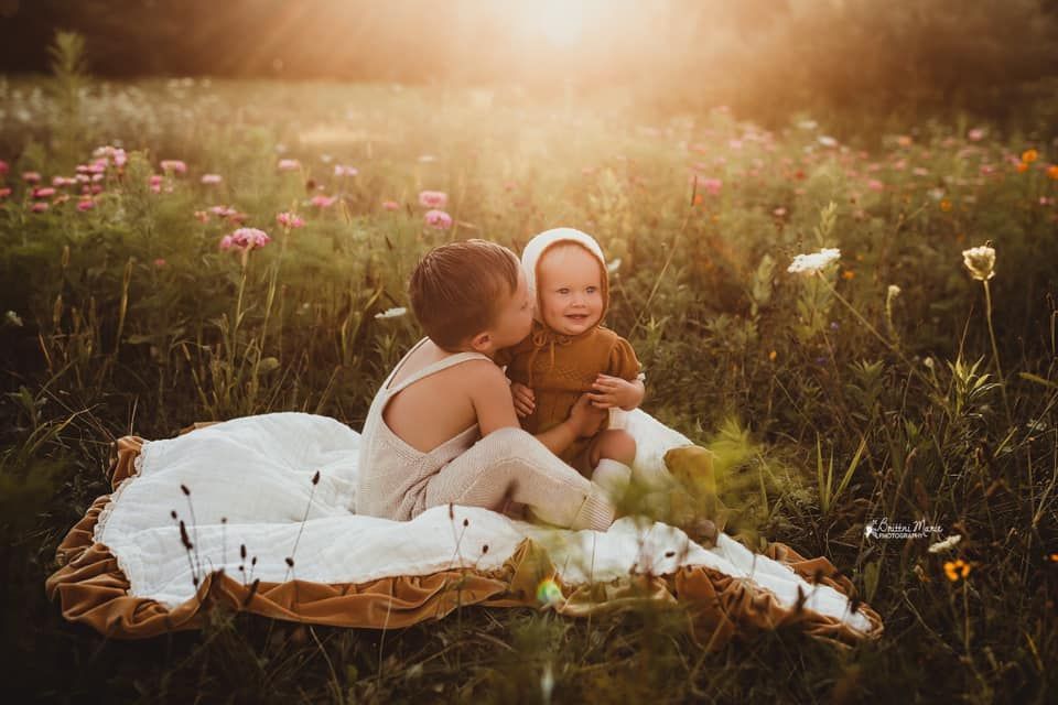 Two children are sitting on a blanket in a field of flowers.