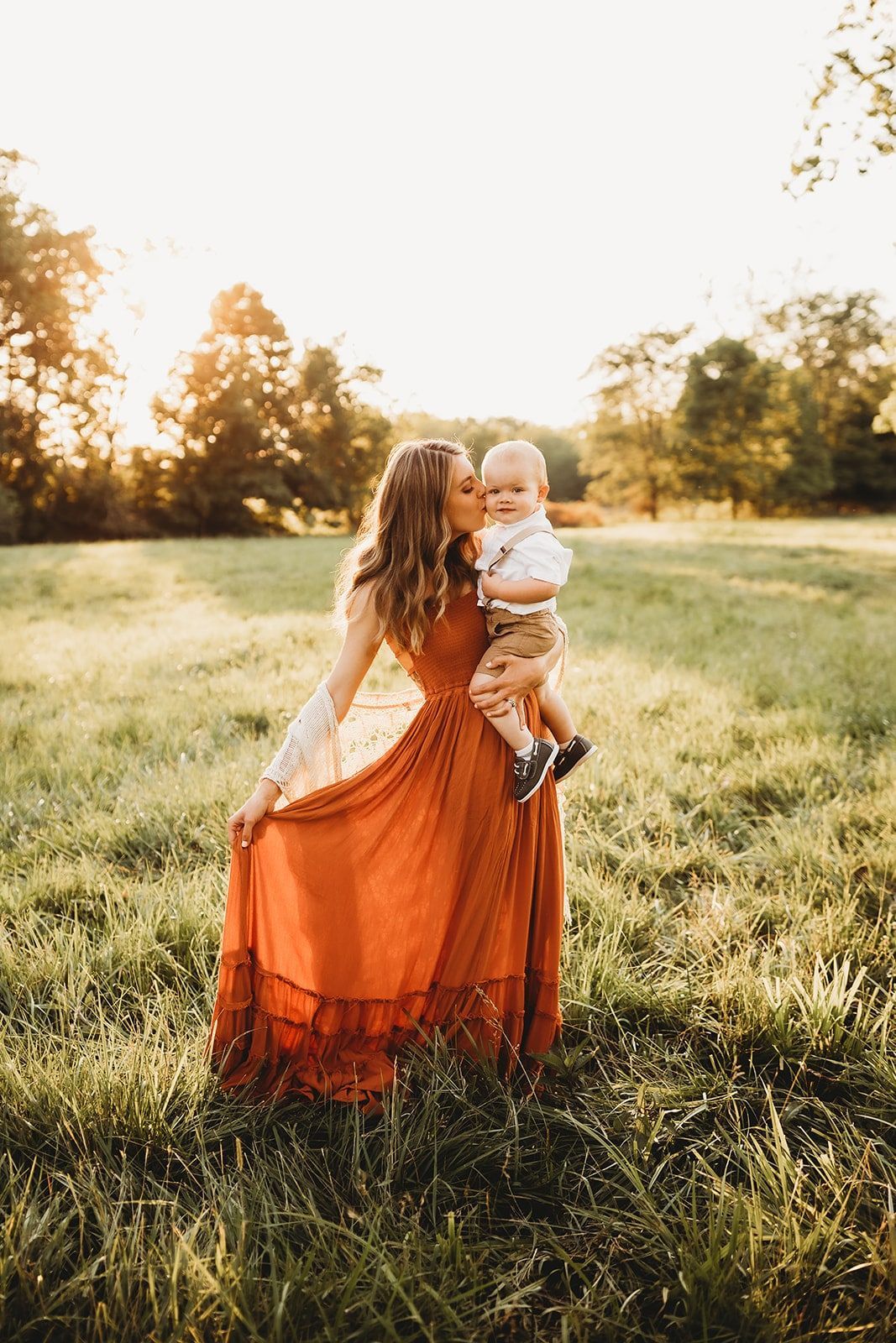 A woman in an orange dress is holding a baby in a field.