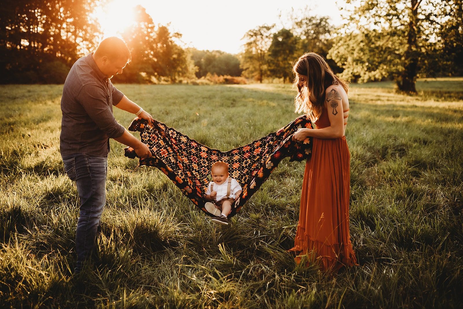 A man and a woman are holding a baby in a field.