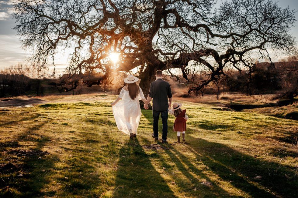 A family is walking in a field with a tree in the background.