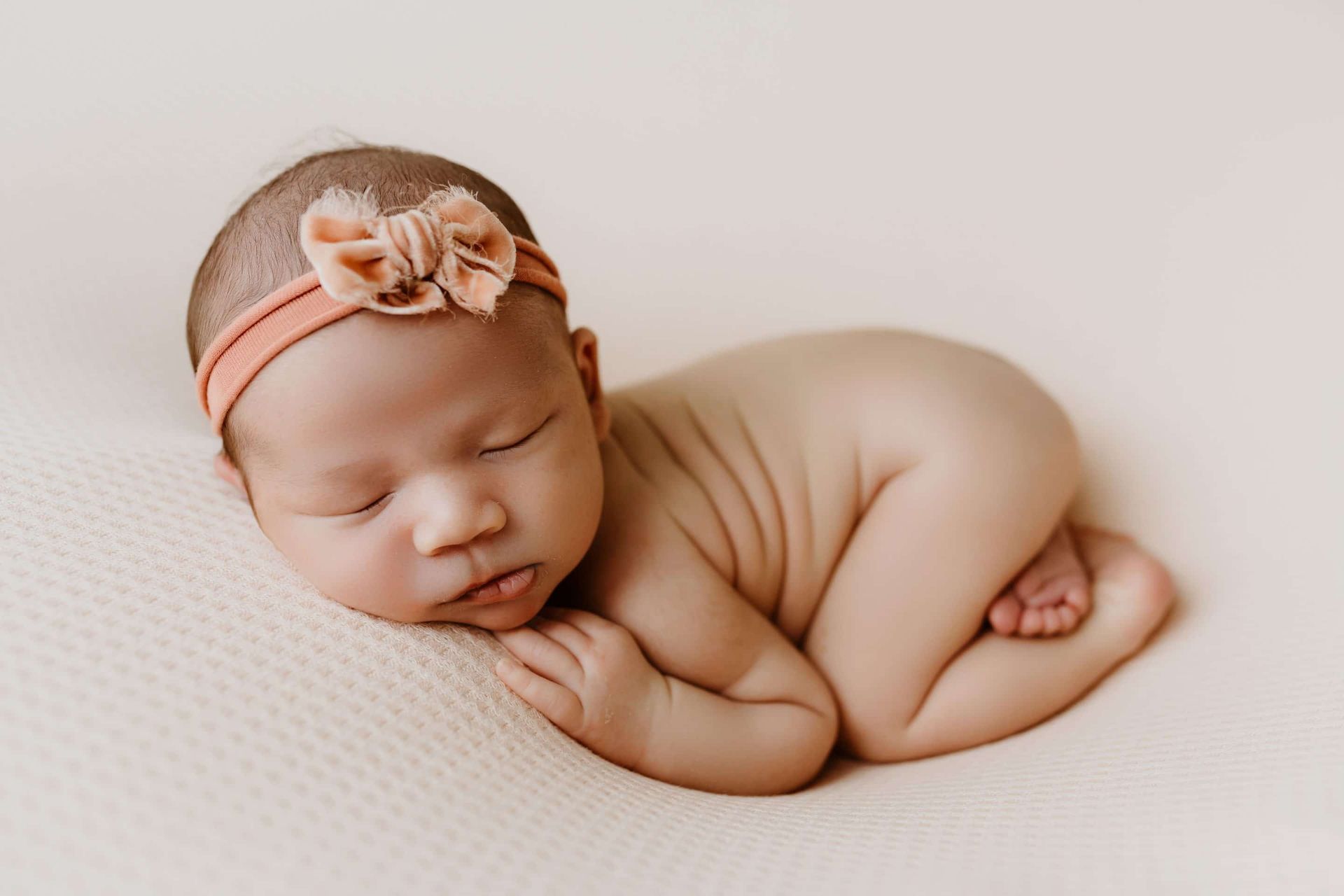 A newborn baby girl wearing a headband is sleeping on a blanket.
