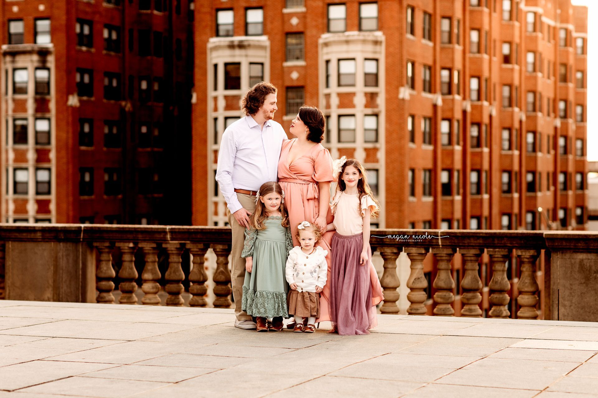 A family is standing on a balcony in front of a brick building.