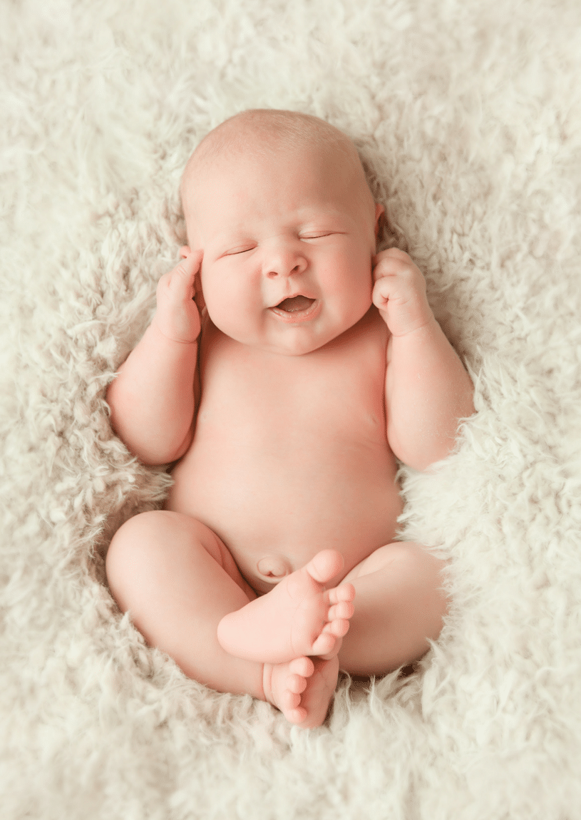 A newborn baby is laying on a white blanket and smiling.