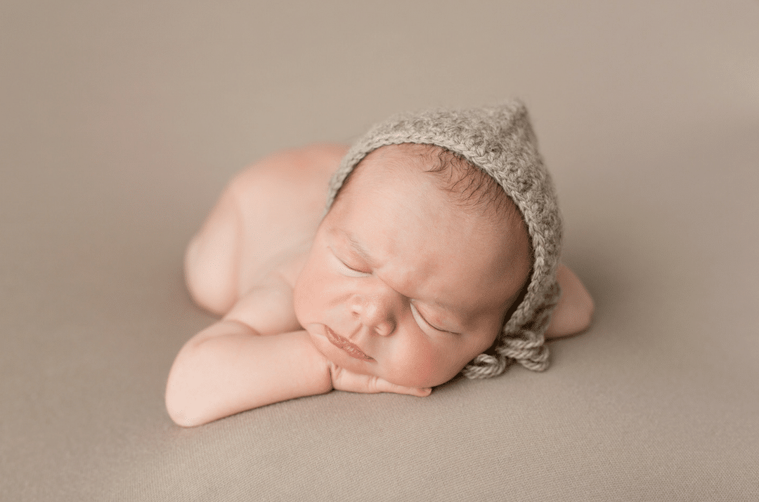 A newborn baby wearing a knitted hat is sleeping on a blanket.