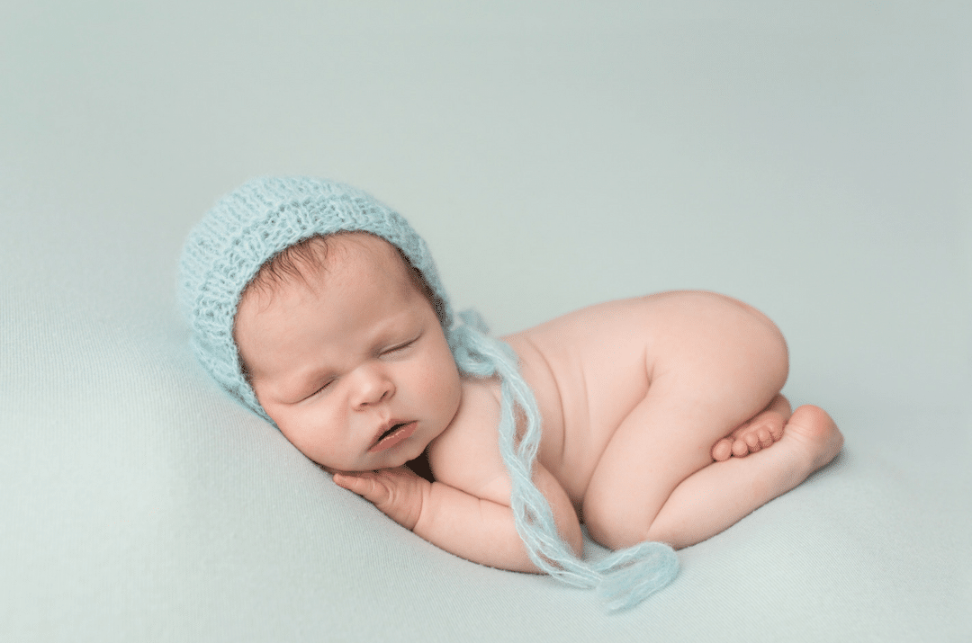 A newborn baby wearing a blue hat is sleeping on a blue blanket.