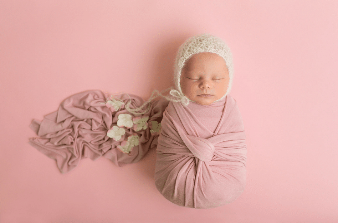 A newborn baby wrapped in a pink blanket and a white hat.