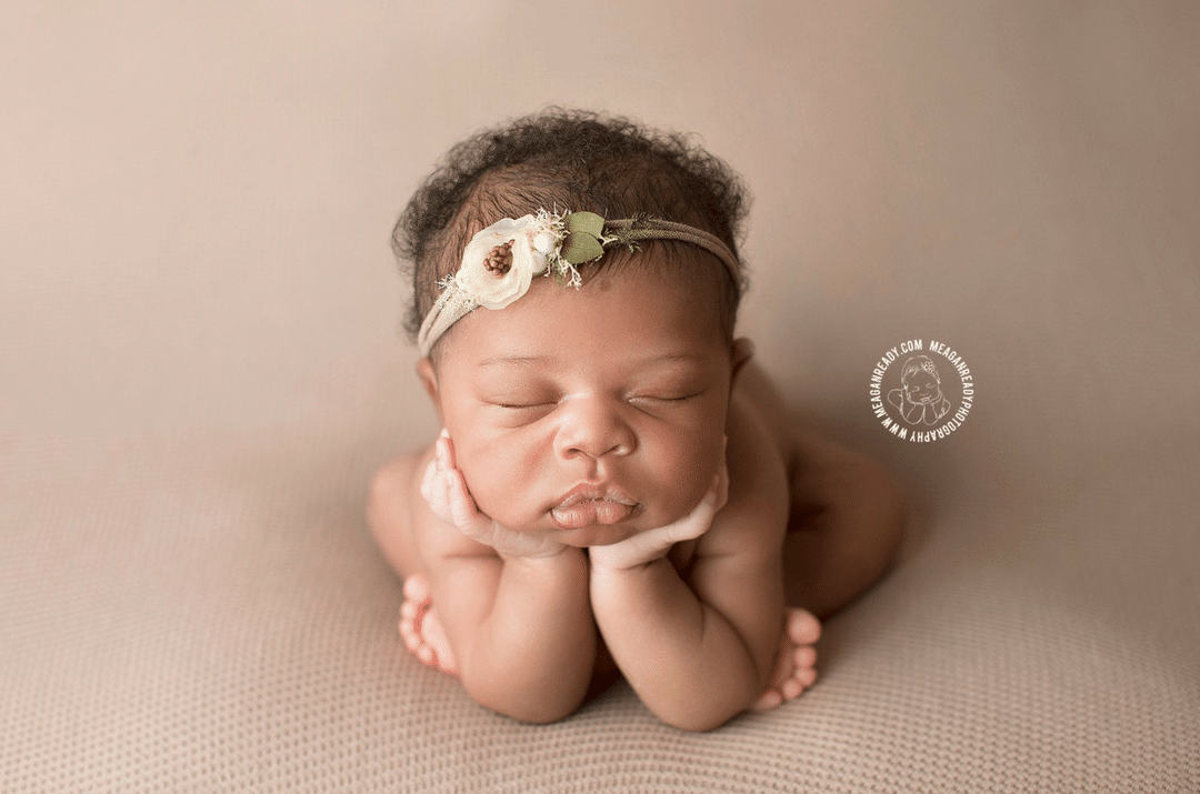 A newborn baby girl is laying on her stomach with her head on her hands.
