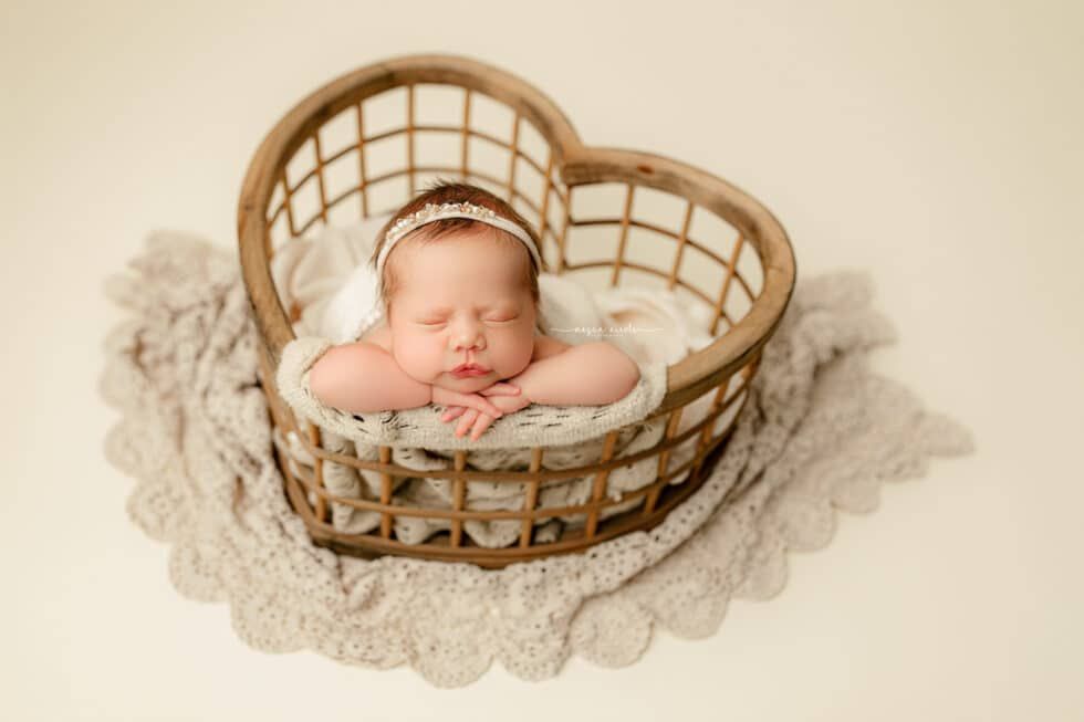 A newborn baby is sleeping in a heart shaped basket.