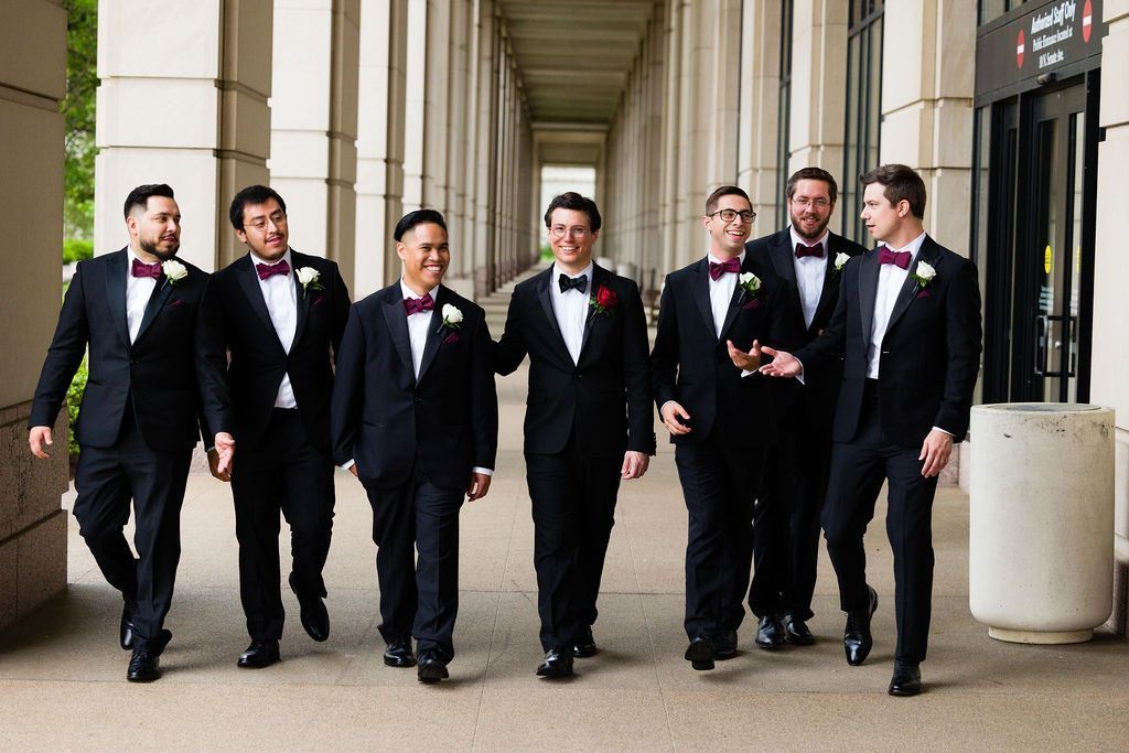 A group of men in tuxedos and bow ties are walking down a hallway.