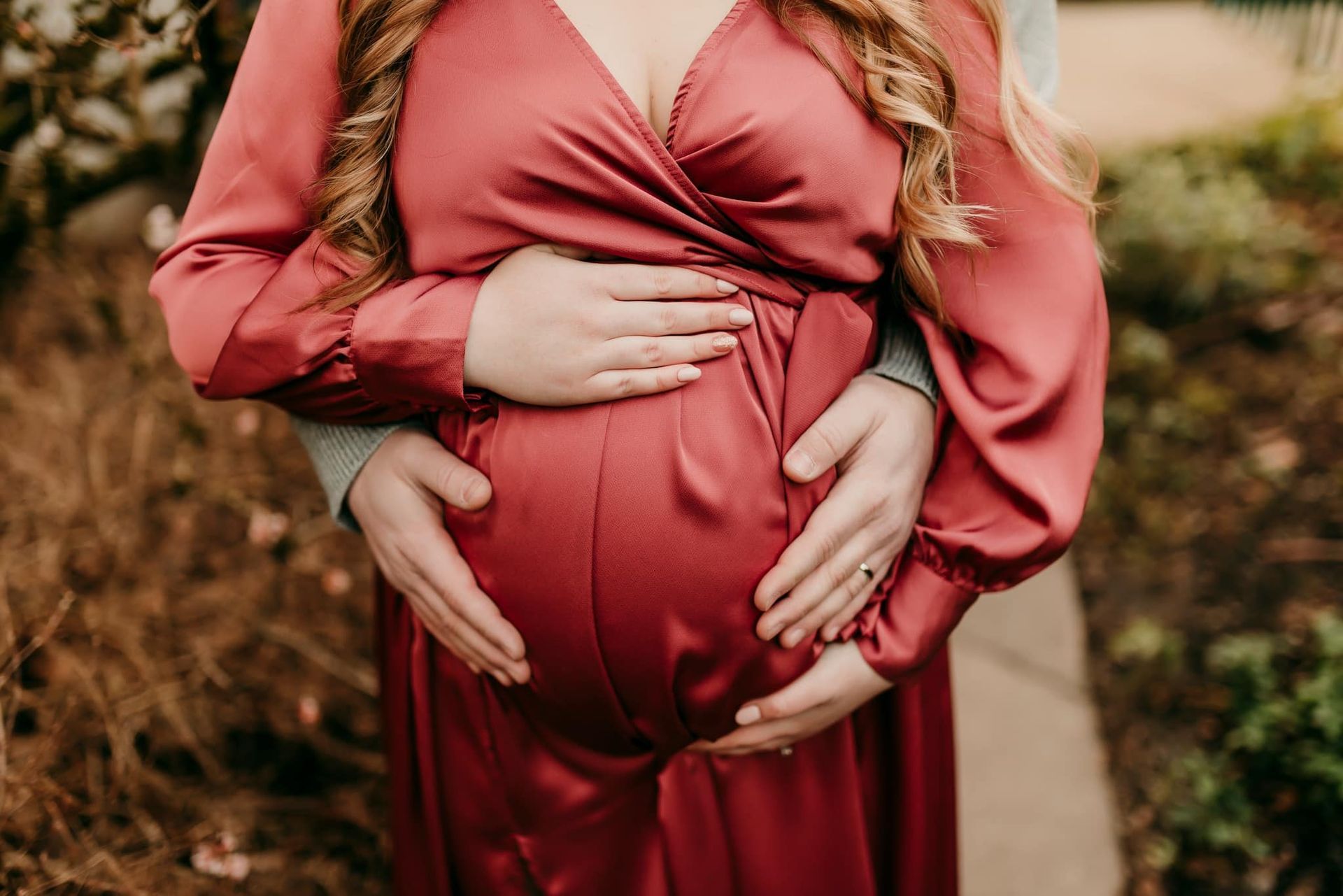 A pregnant woman in a red dress is standing next to a man holding her belly.