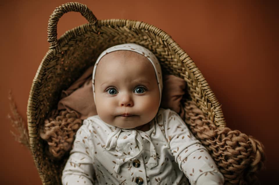 A baby is sitting in a wicker basket and looking at the camera.