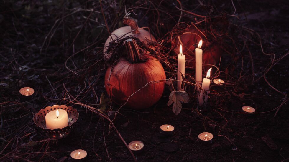 A pumpkin and candles are sitting on the ground in the dark.