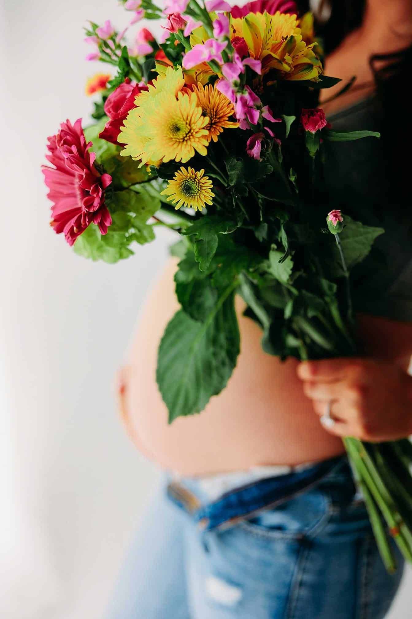 A pregnant woman is holding a bouquet of flowers in front of her belly.