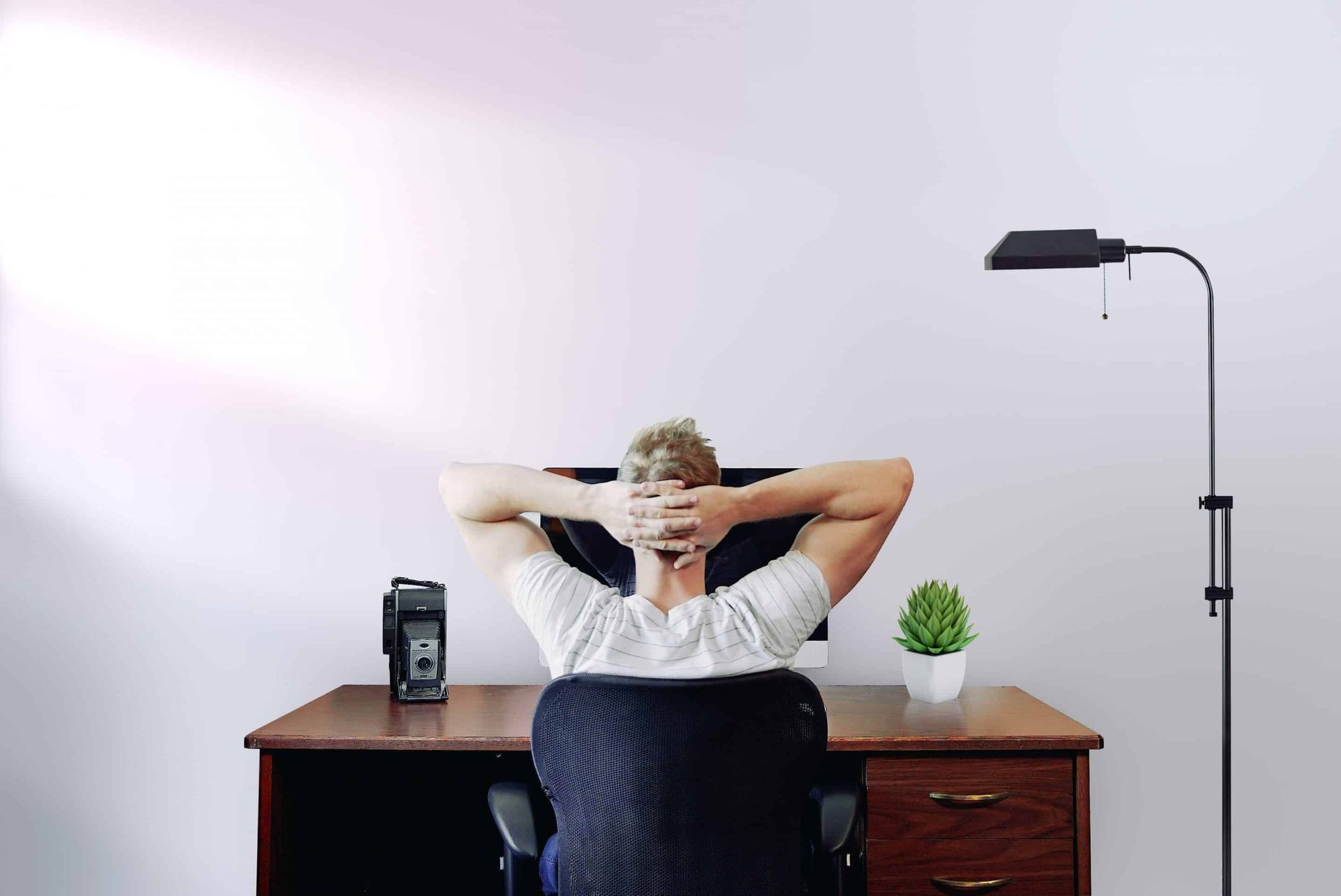 A man is sitting at a desk with his hands behind his head.