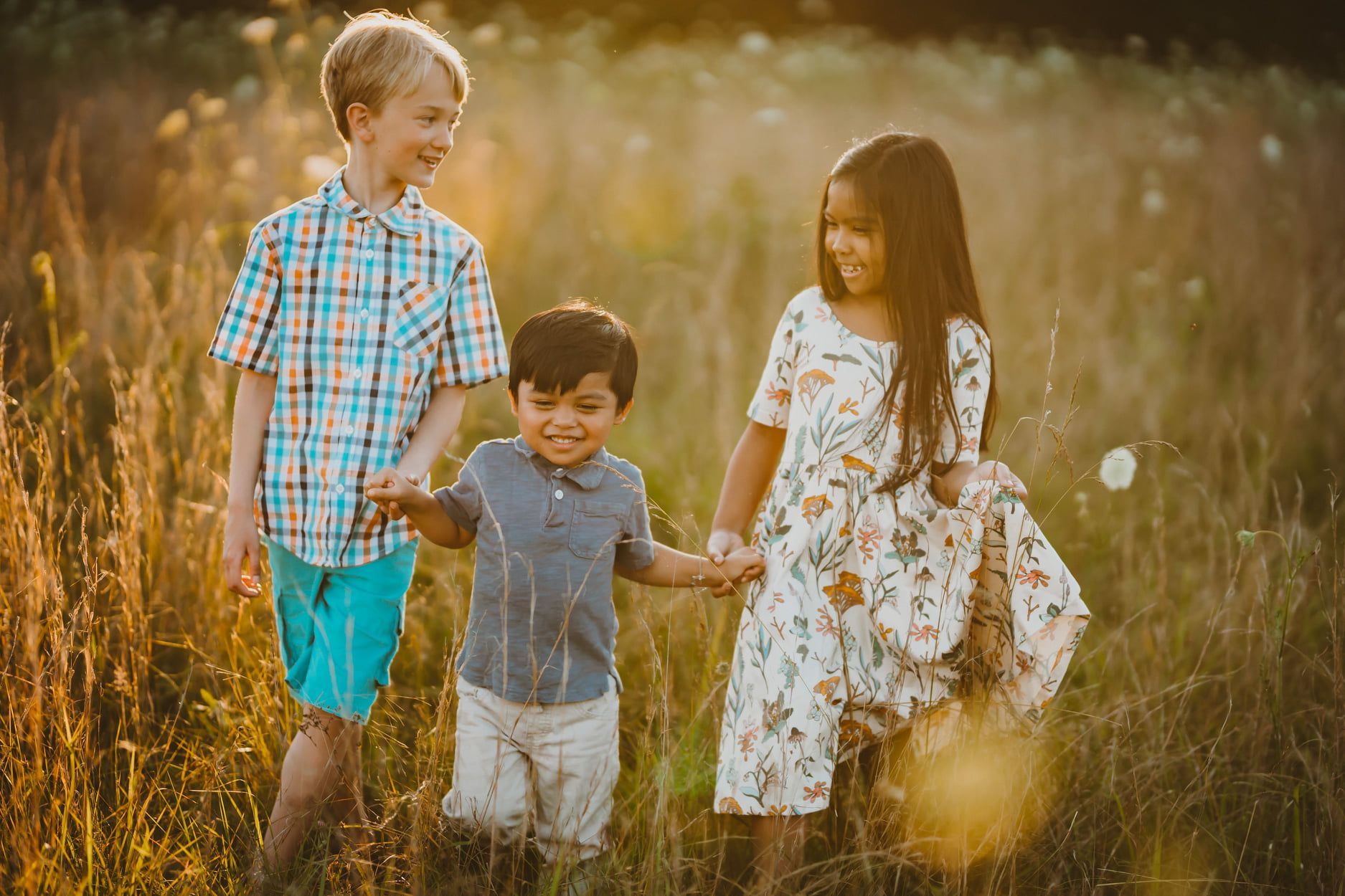 Three children are walking through a field holding hands.
