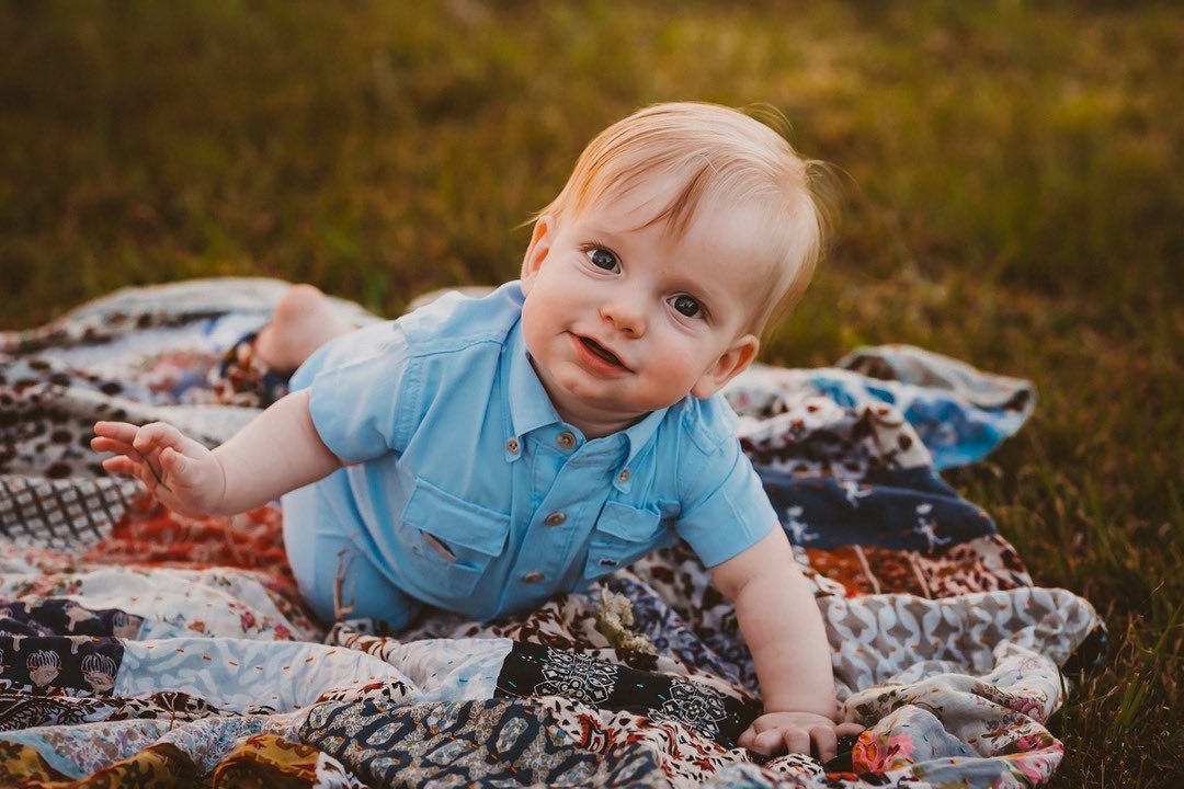 A baby is laying on a blanket in the grass.