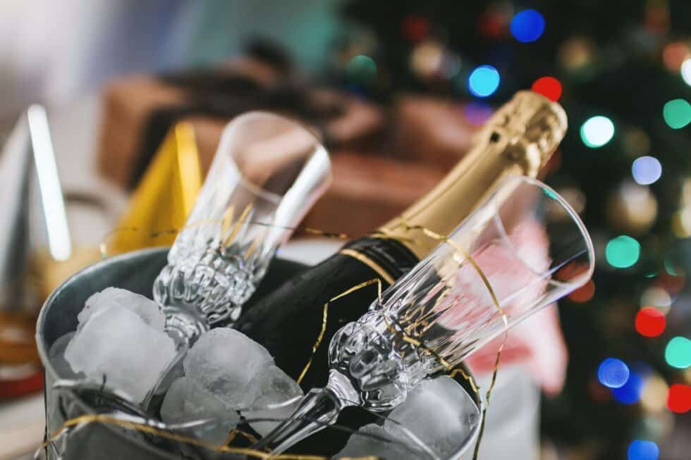 A bucket of ice with a bottle of champagne and two glasses in it.