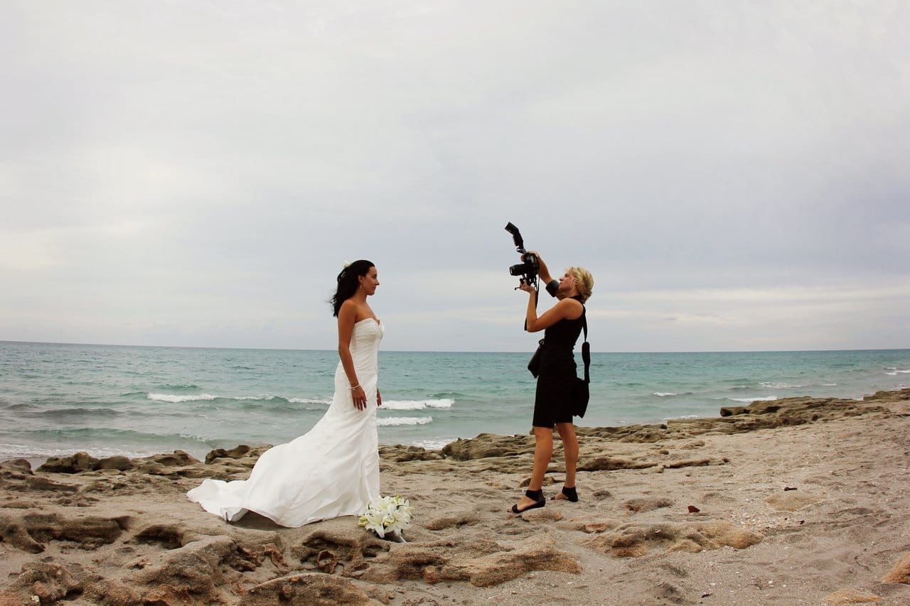 A woman is taking a picture of a bride on the beach.