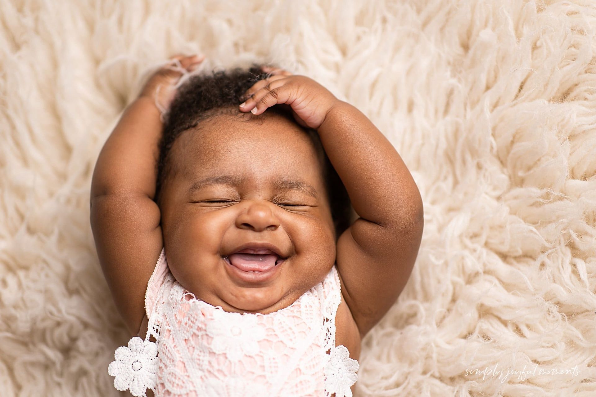 A baby is laying on a blanket and smiling.
