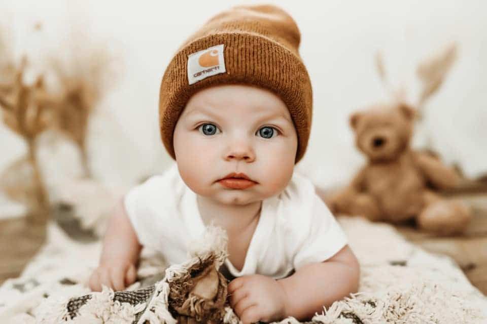 A baby wearing a brown beanie is laying on a blanket.