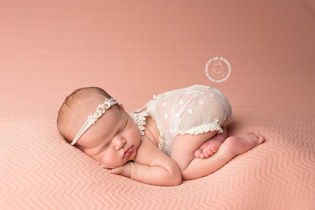 A newborn baby girl is laying on her stomach on a pink blanket.