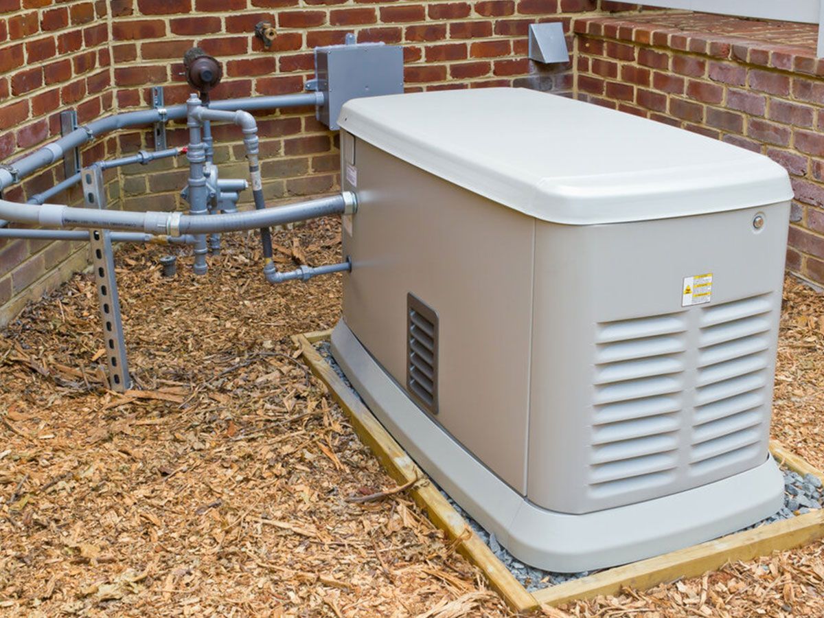 A generator is sitting on the ground in front of a brick building.