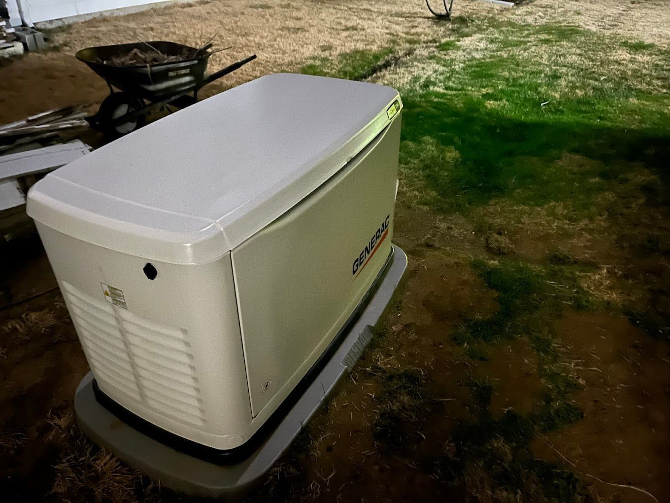 A white generator is sitting on the ground in a yard.