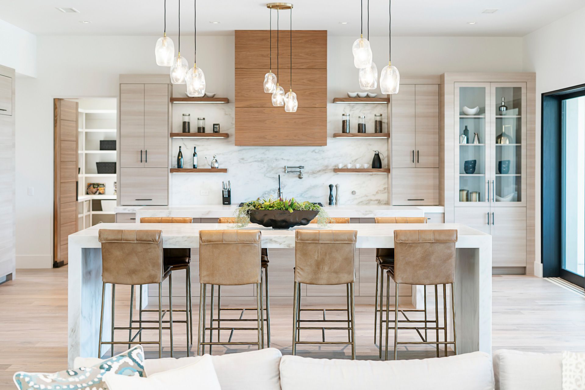 A kitchen with a large island and stools in a living room.