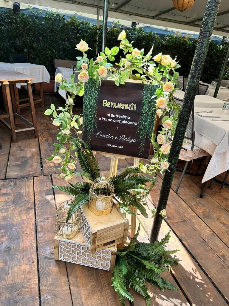 Cartello con fiori su un cavalletto di legno, per dare il benvenuto a un evento, all'aperto su un patio.