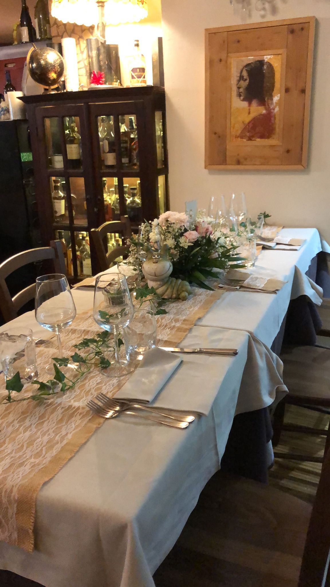 Tavolo da pranzo formale apparecchiato per un pasto, con centrotavola floreale e opere d'arte incorniciate.