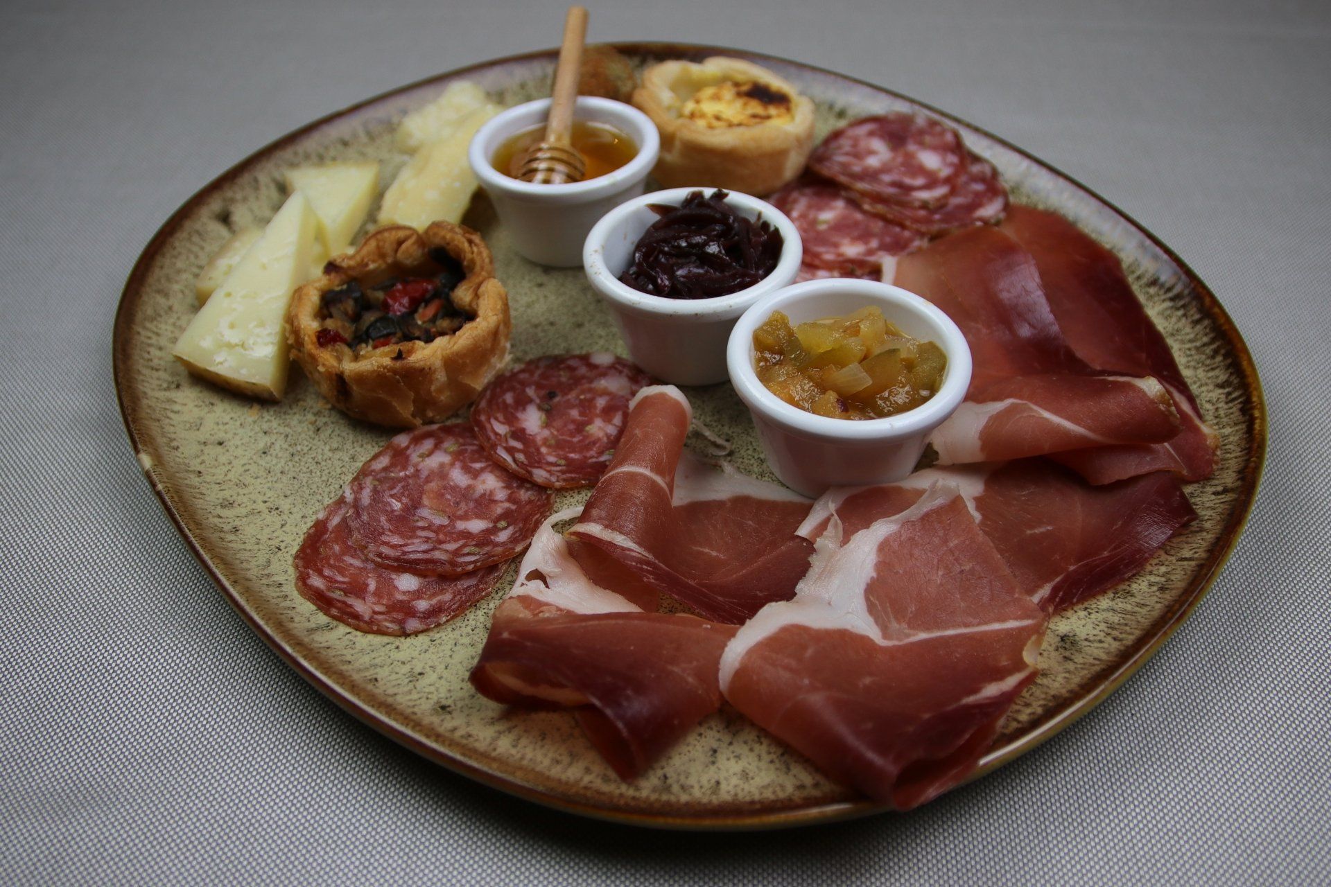 Tagliere di salumi con carni, formaggi e piccoli piatti di miele, chutney e marmellata.