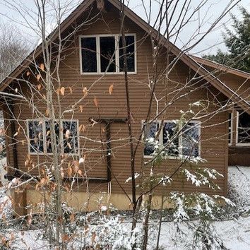 A wooden house with snow on the ground and trees in front of it.