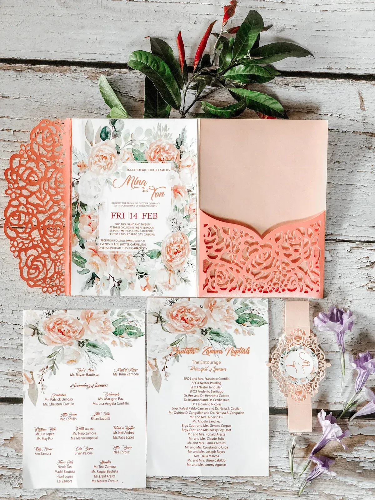 Coral floral wedding invitations laid on rustic wood.