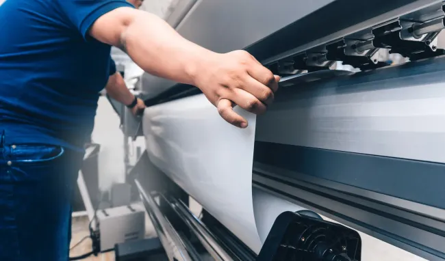 Person operating a large format printer, loading white material.