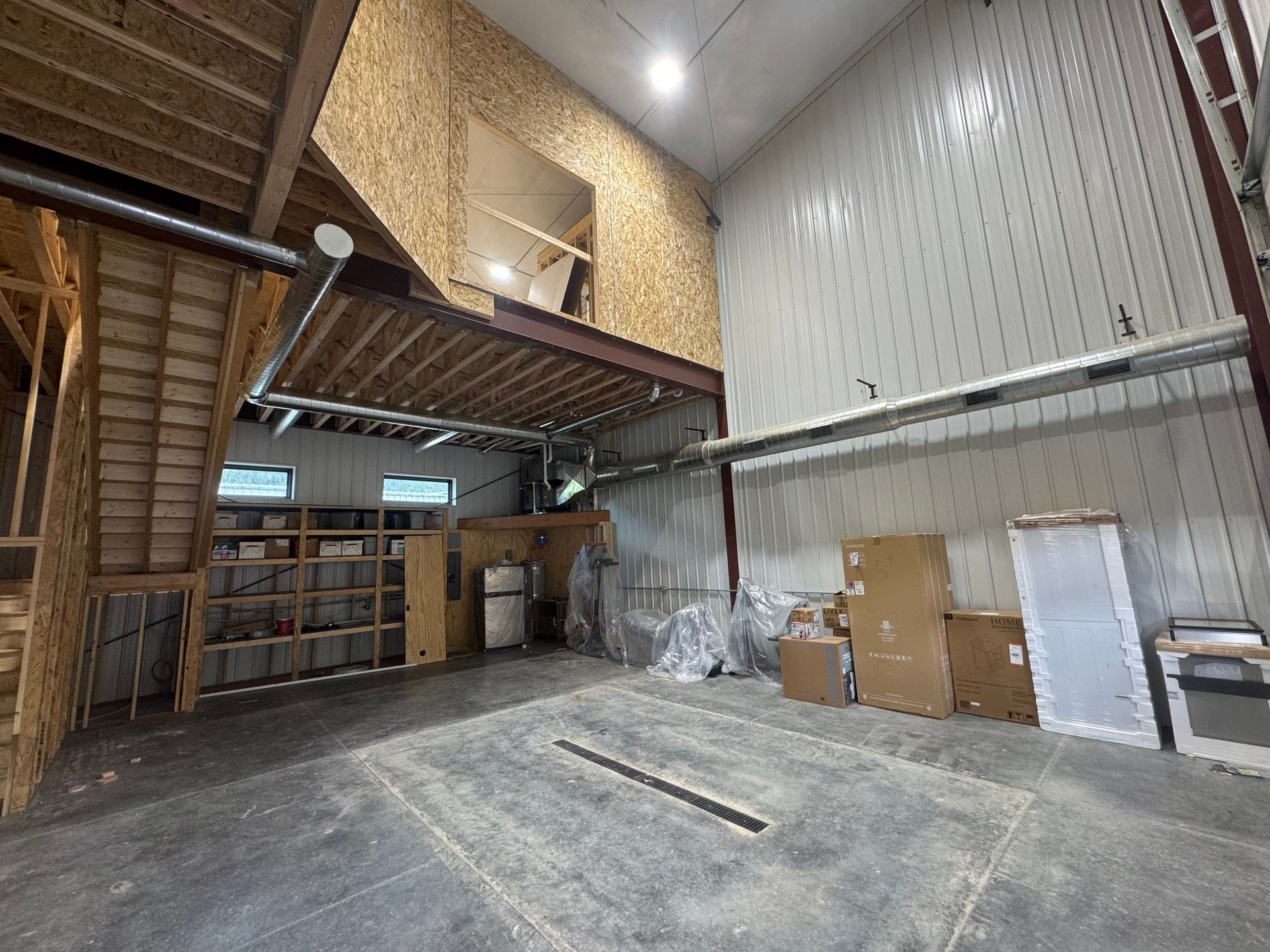 Empty warehouse interior with mezzanine, metal walls, concrete floor, and stacked pallets along the back wall