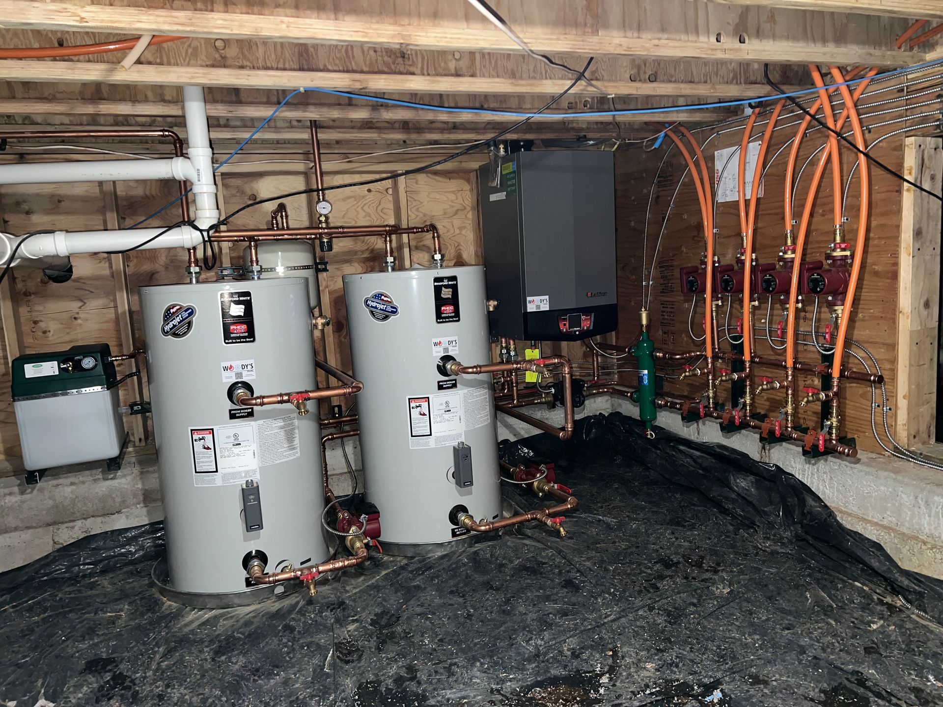 Utility room with two white water heaters, exposed pipes, and orange tubing on a dirt floor.